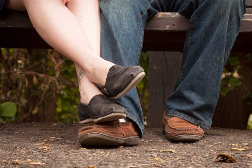 Happy couple relaxing on park bench, crossing legs