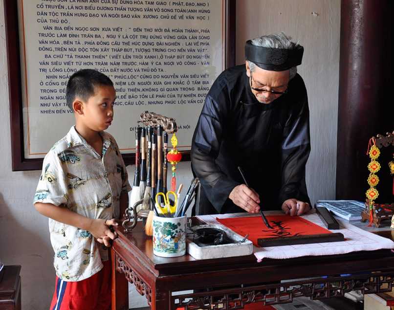 Elderly man showing a young man how to paint asian characters