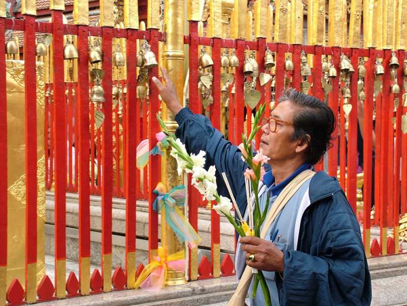 Man ringing prayer bells and holding flowers in Thailand