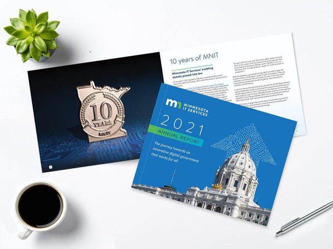 Minnesota IT Services 2021 annual report sitting on desktop with pen and cup of coffee.