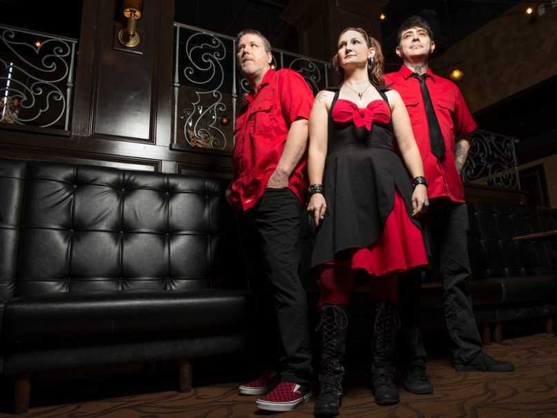 Band in matching red clothing in front of dark alt background